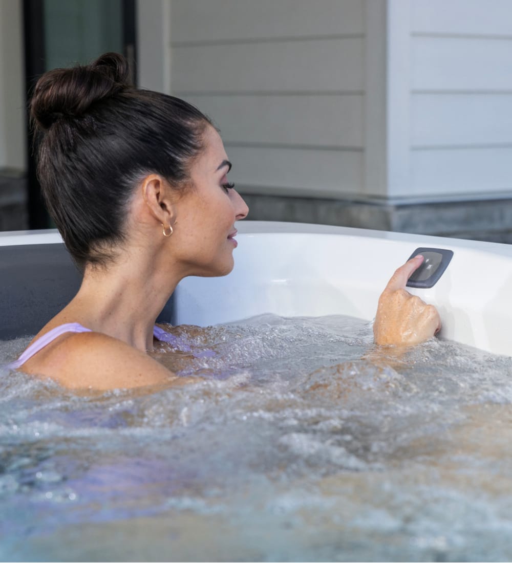 A woman is sitting in a hot tub pushing buttons on the edge of the machine.